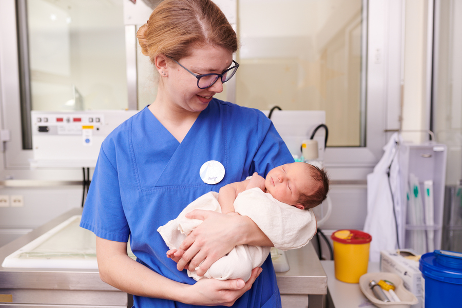 Pflegerin der Frauenklinik hält Neugeborenes im Kreisssaal im Arm